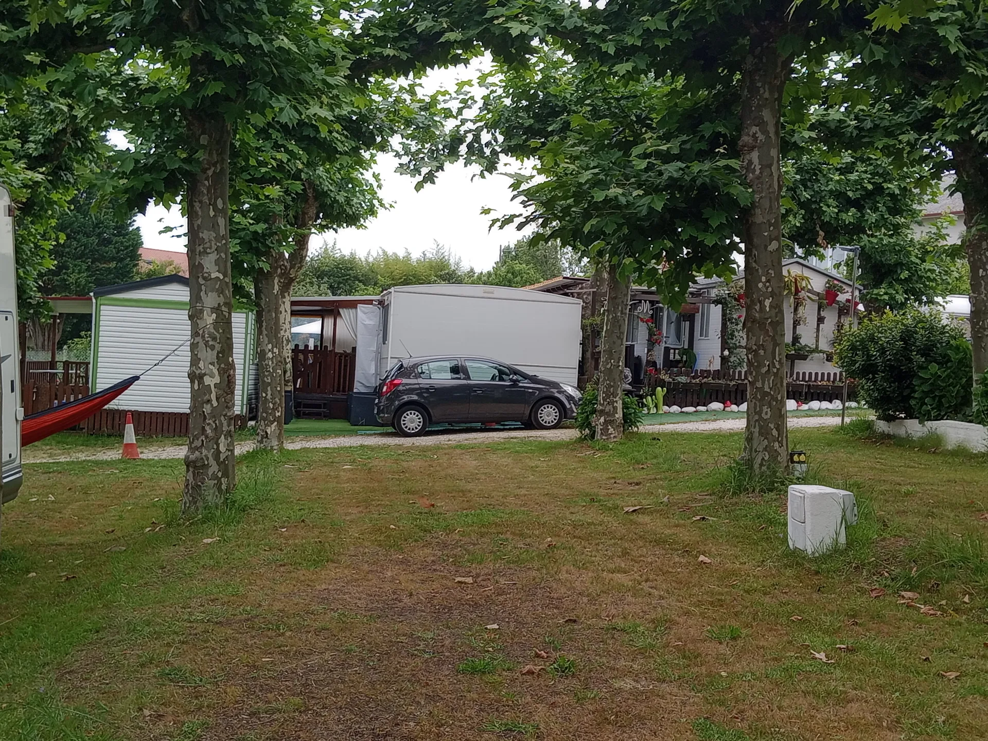 Parcelas arboladas del camping con vehículos y caravanas.