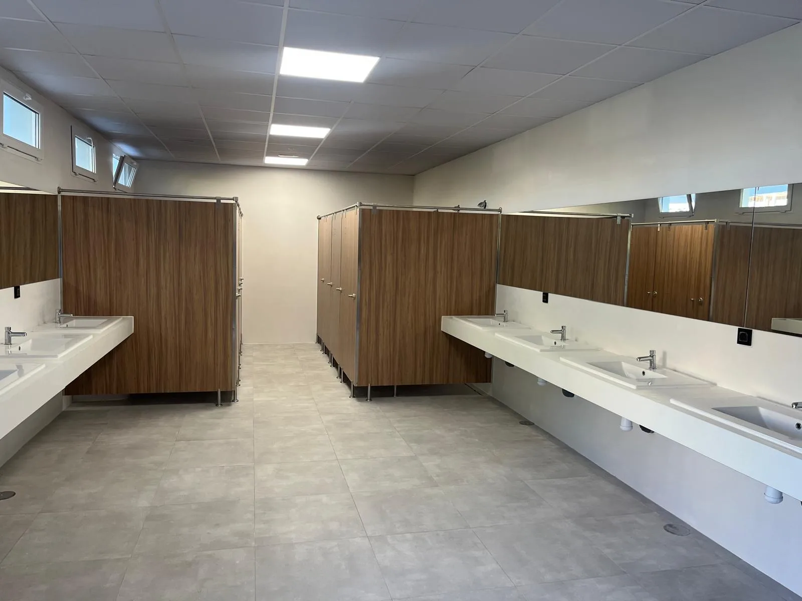 Bloque de baños y duchas de Camper Park Alicante con lavabos, espejos y cabinas de madera