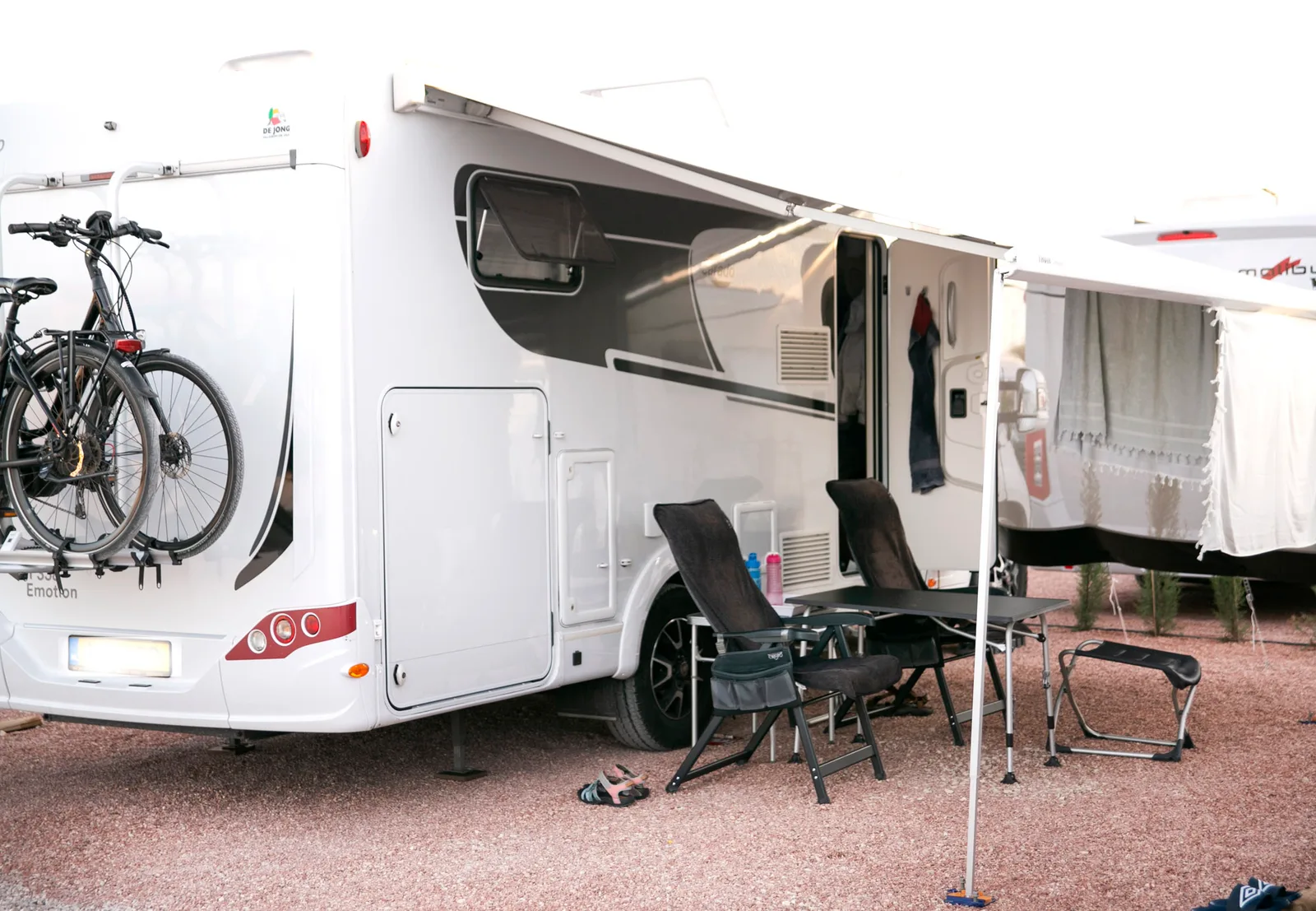 Autocaravana estacionada en una parcela del camper park con el toldo desplegado, mesa y sillas