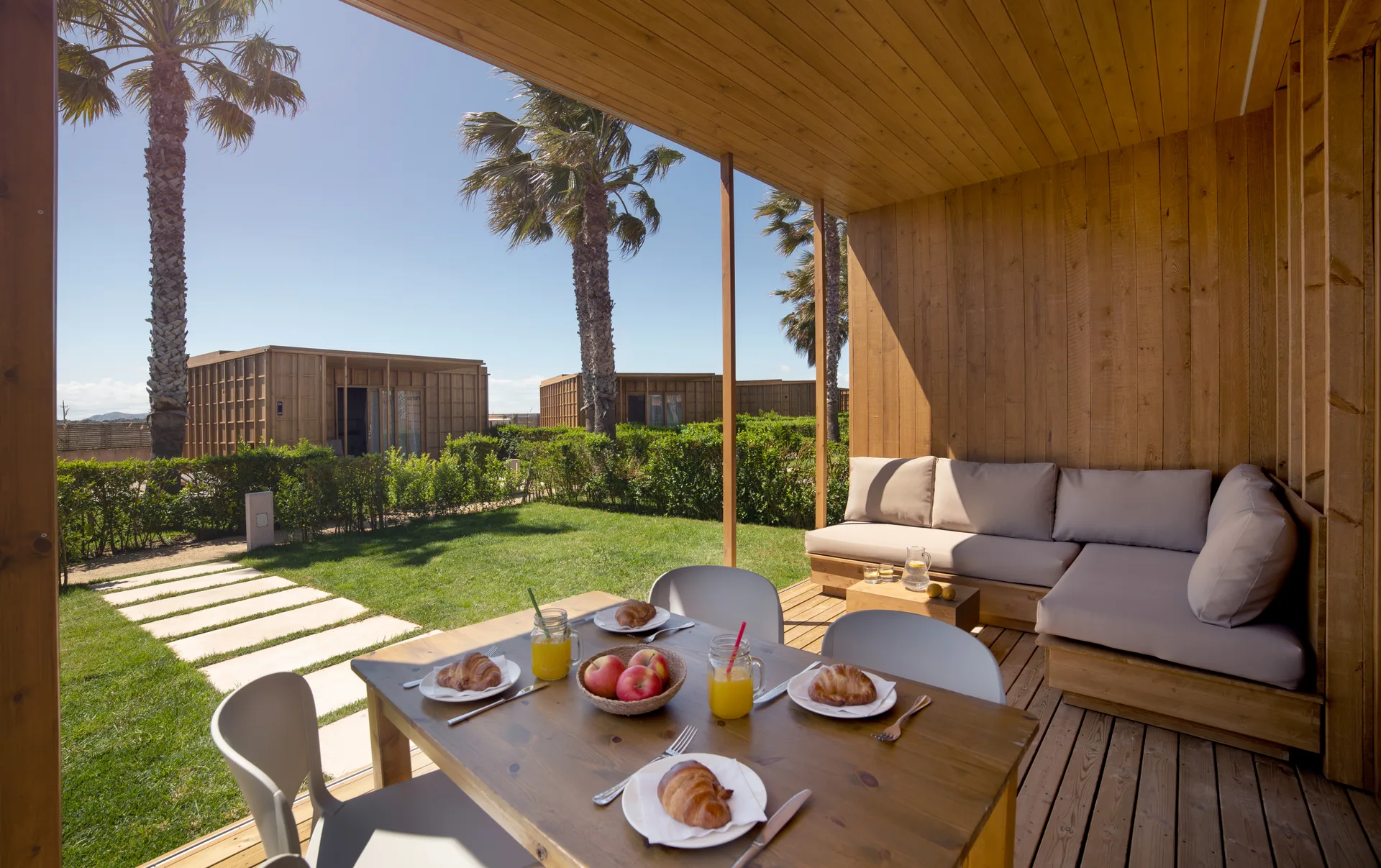 Terraza de alojamiento con mesa puesta y vistas a bungalós y palmeras del camping.
