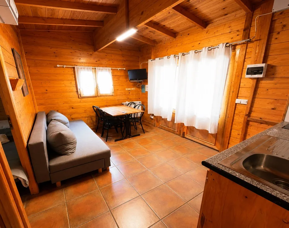 Interior de una estancia común del camping, tipo salón-cocina, con mesa, sofá y fregadero.