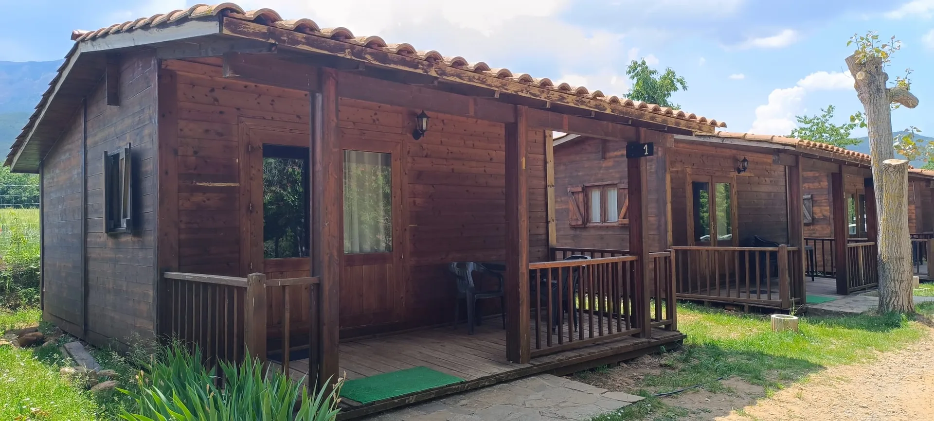 Bungalows de madera del camping con porches, en exterior y con entorno ajardinado.