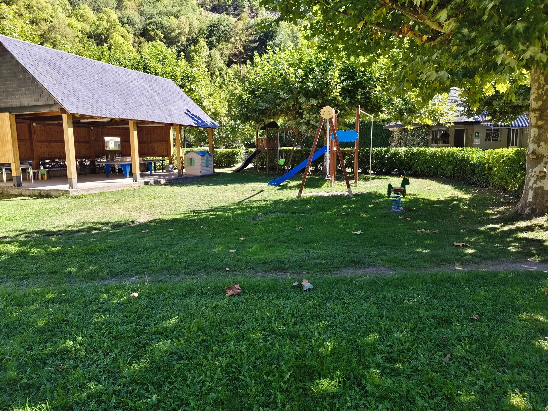 Zona común del camping con parque infantil y merendero, rodeada de vegetación.