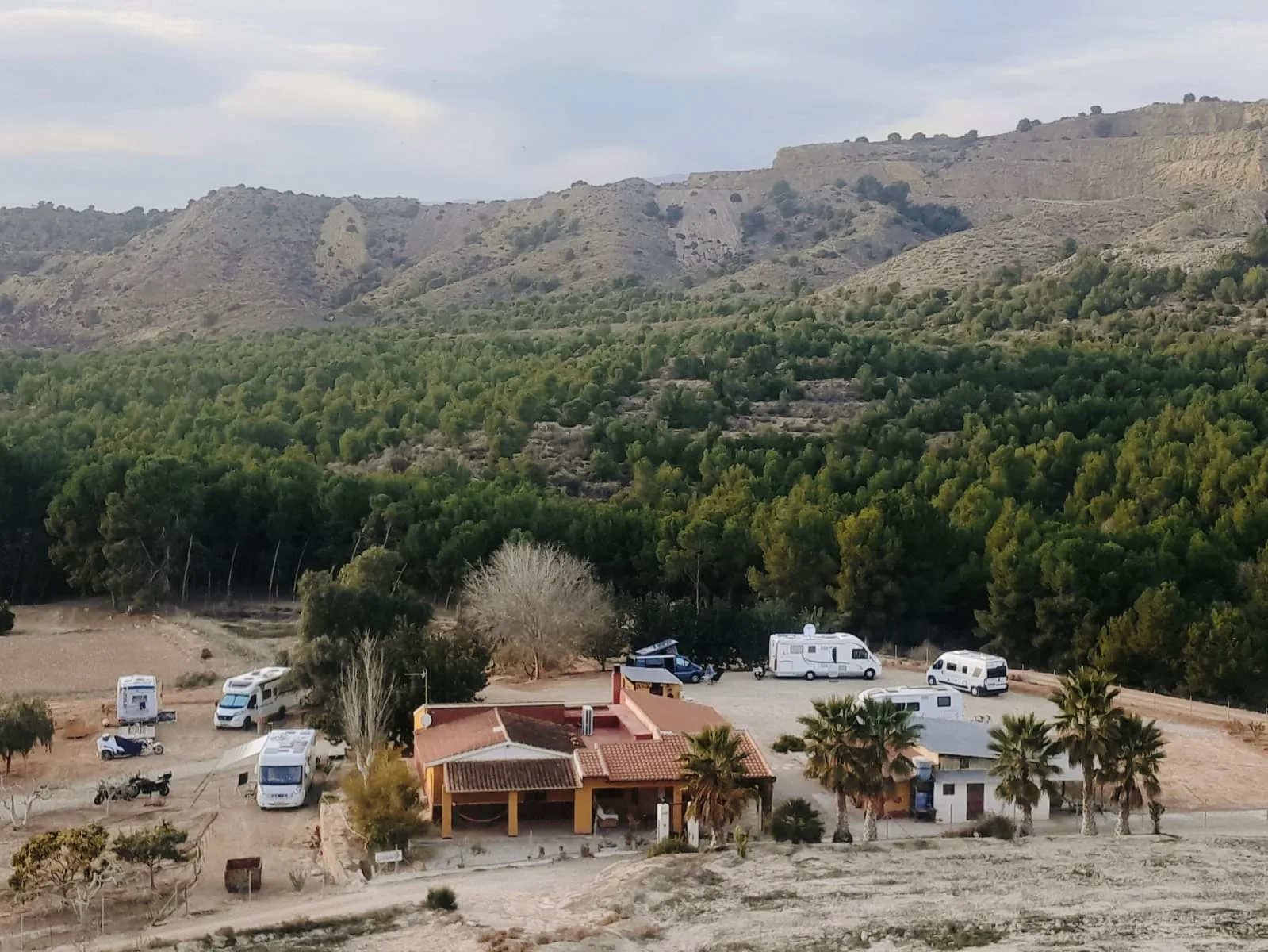 Vista general del área de la Granja La Carmela con autocaravanas junto a la casa, entre pinar y sierra