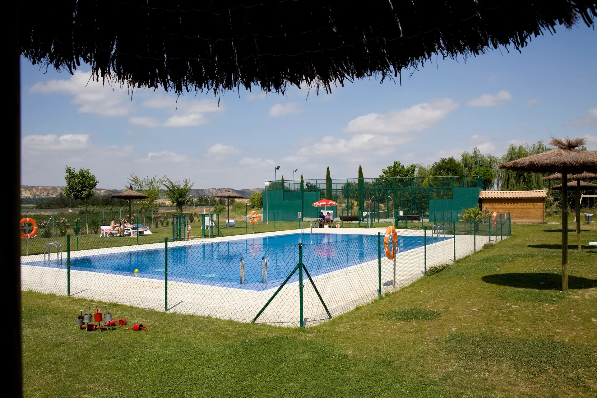 Piscina exterior de camping con zona ajardinada y sombrillas.