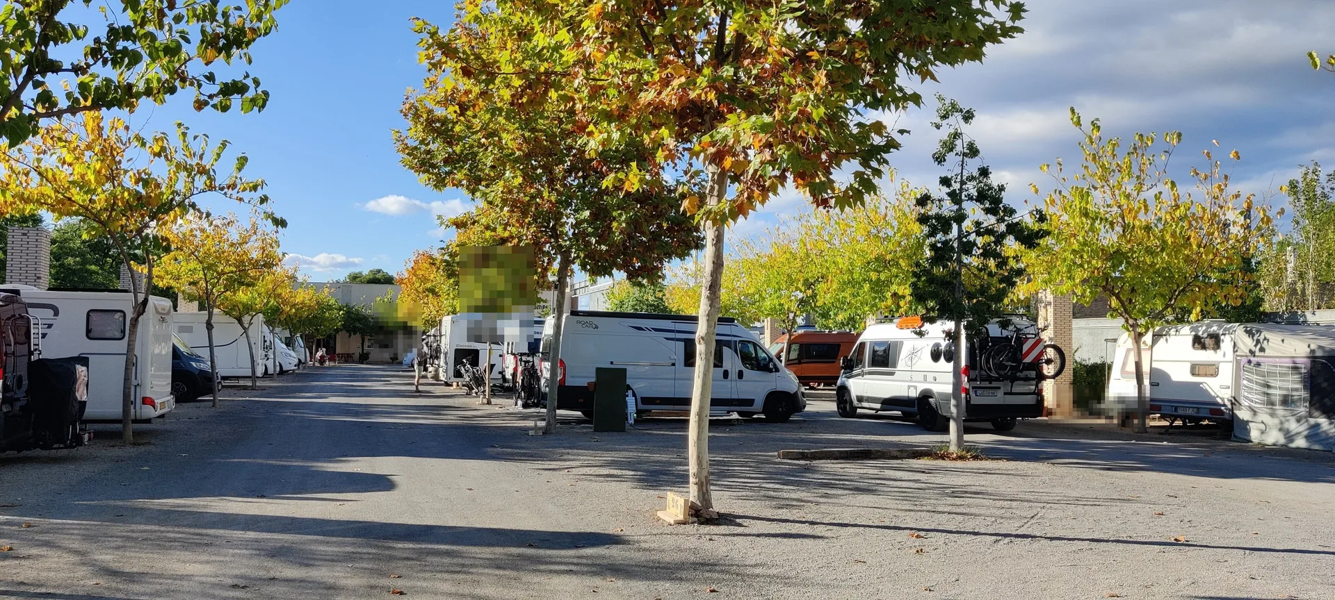 Área de autocaravanas con parcelas arboladas y varias campers estacionadas.