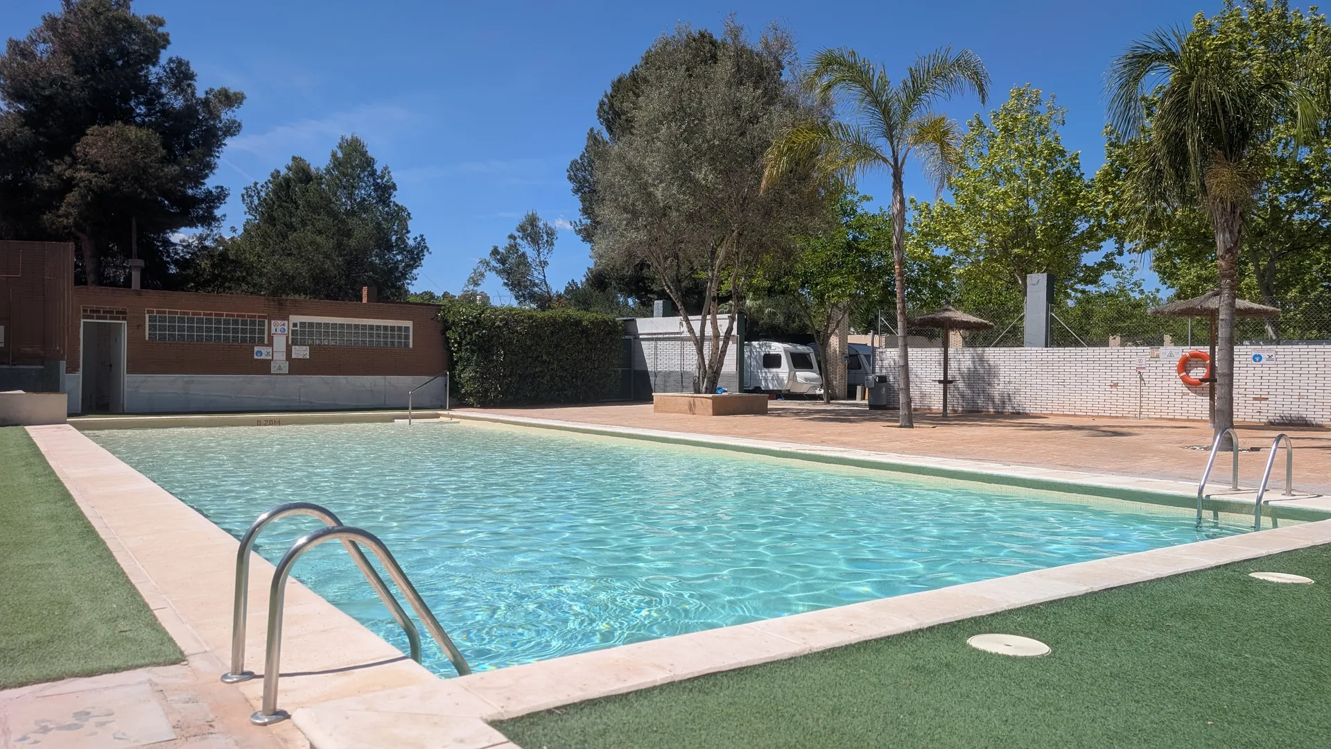 Piscina exterior y zona común del camping con caravanas al fondo.
