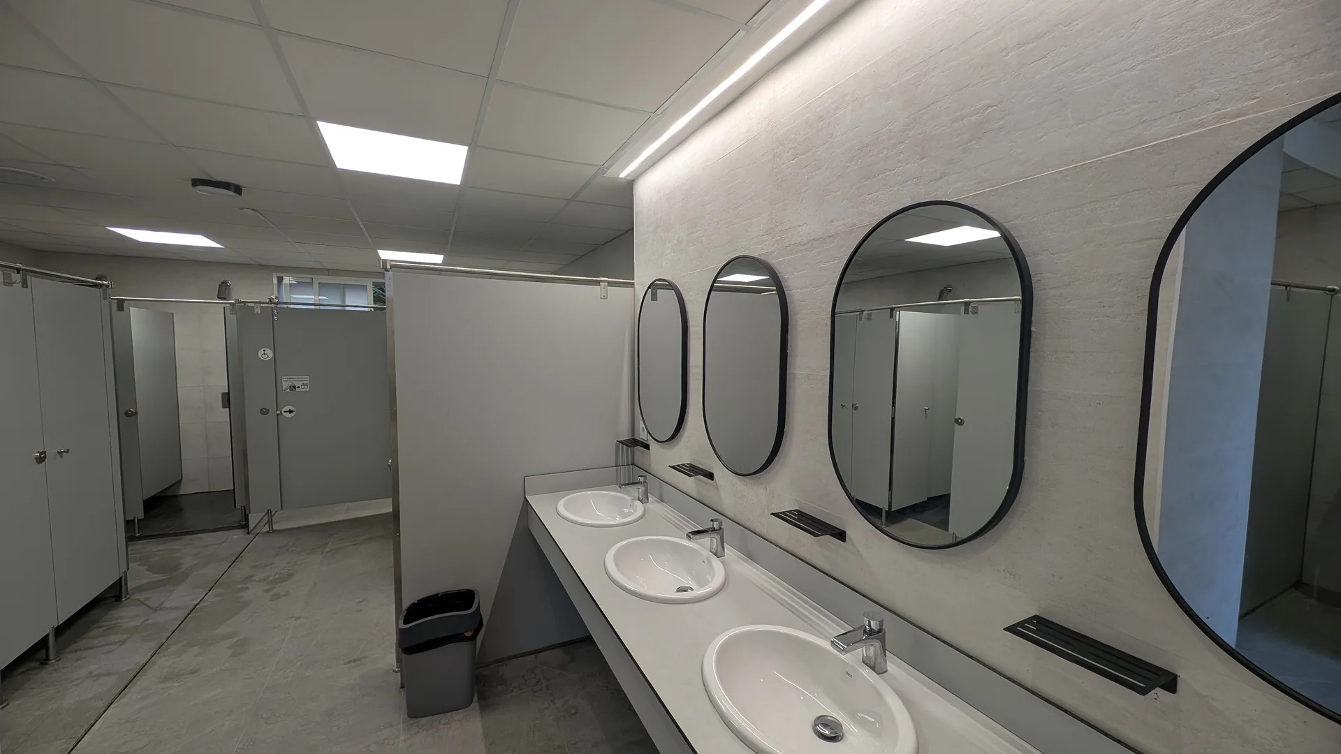 Aseo interior moderno con lavabos, espejos y cabinas de ducha/baño.